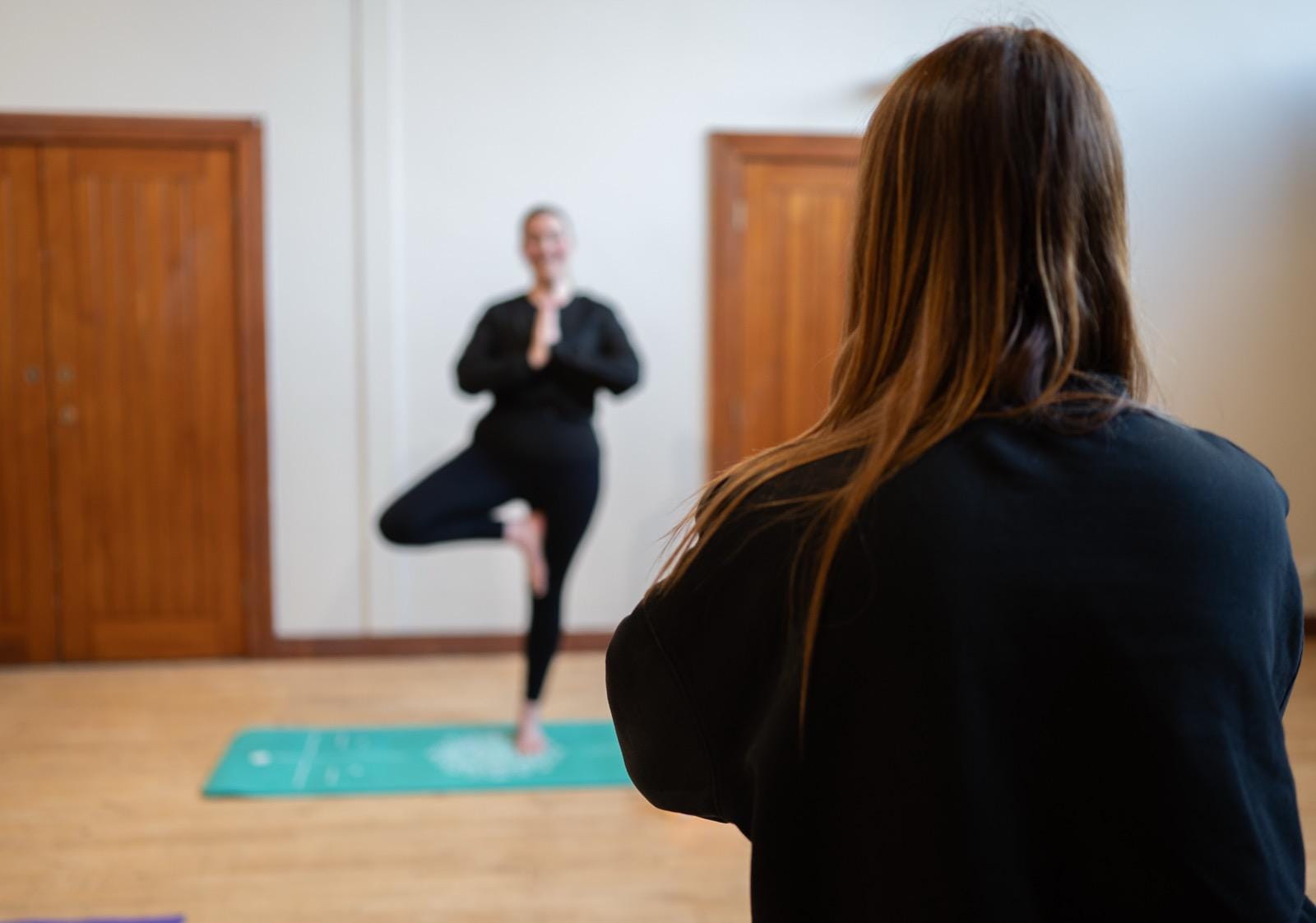 Learner watches instructor in tree pose on teal mat in a training room — counselling training and wellbeing, Liverpool.