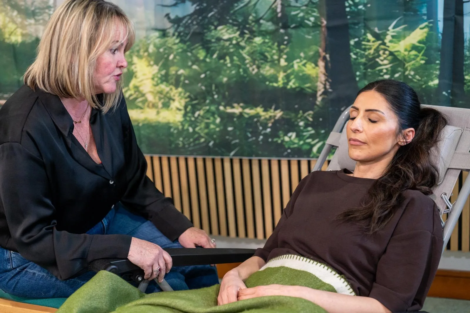 Therapist talking to a reclining client with eyes closed, green blanket, forest mural backdrop, hypnotherapy training in Liverpool.