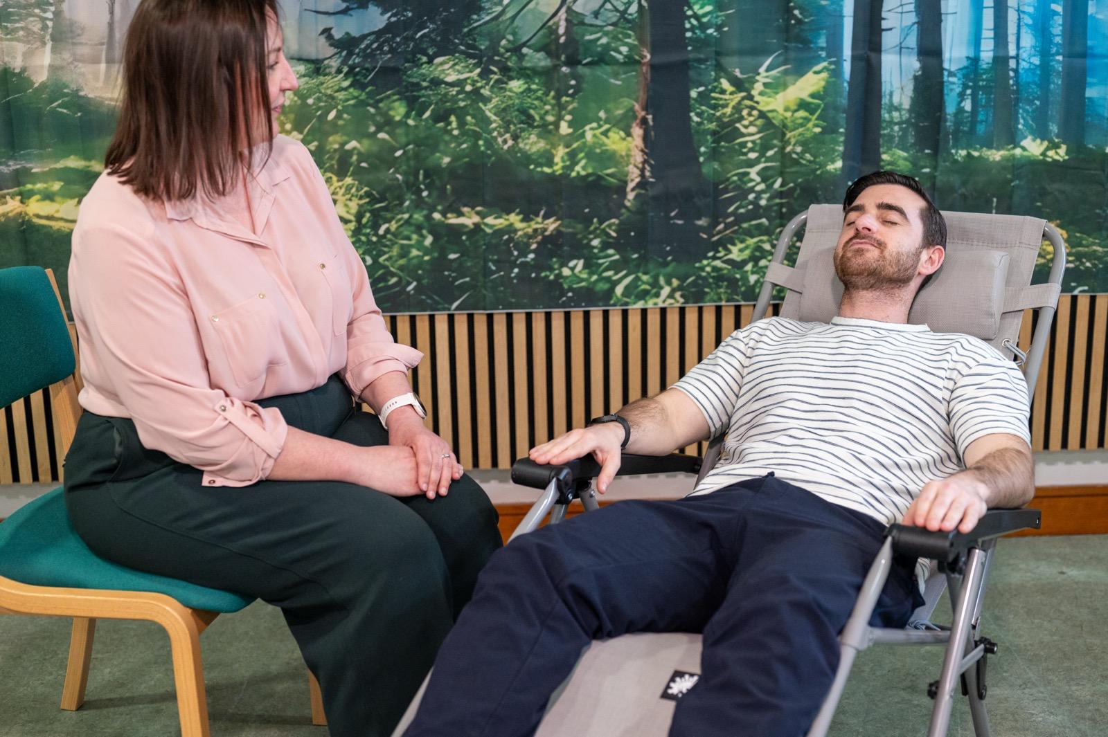 Therapist trainee beside a man reclining in a striped top during Liverpool hypnotherapy training, forest backdrop